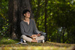 © Prathankarnpap - Relaxed asian man enjoy listening music and reading book under the tree in the park