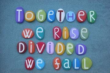 Together we rise, divided we fall, creative quote composed with multi colored stone letters over green sand