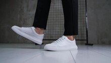 Stylish Snow-white Sport Shoes With Laces On A Model. Man Wearing Black Trousers And Modern Sneakers Posing In Studio. Close Up.