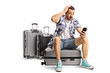 © Ljupco Smokovski - Shocked male tourist sitting on a suitcase and looking at a smartphone