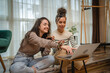 © Dusan - Two friends or sisters or girlfriends are sitting on the ground watching on laptop what to buy online while smiling and talking and drinking coffee in their apartment