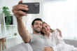 © Basicdog - Caucasian couple video calling talking with friends on mobile phone in living room.