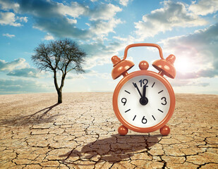 Wall Mural - Alarm clock with five minutes before twelve o'clock on arid cracked soil. Concept of climate change or global warming.