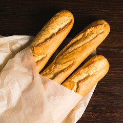 Delicious baguettes from the bakery wrapped in baking paper, on a dark wooden background