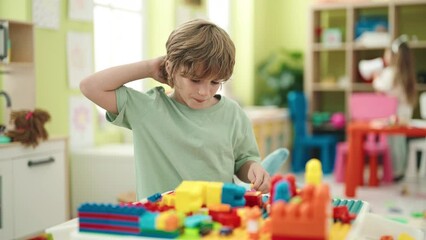 Poster - Adorable caucasian boy playing with construction blocks sitting on table at kindergarten