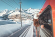 © oatawa - Happy woman traveler looks out from window traveling by train in beautiful winter mountains, Travel concept.