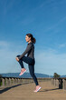 © Rob Wilkinson - Leg stretching exercise fitness runner woman doing running warm-up, hamstring muscles stretch standing wtih single knee to chest stretch. Female athlete preparing legs for cardio workout.