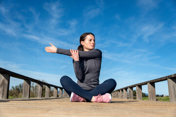 Sporty woman sitting crossed legged doing a shoulder stretch warm up exercise before training outside.