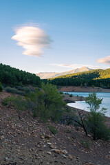 Wall Mural - Beautiful landscape of a lake surrounded by greenery mountains and trees under a blue sky with amazing clouds at sunset, El Vado, Guadalajara, Spain