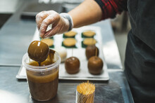 Closeup View Of The Chef's Hand With Gloves Holding An Apple With A Stick And Covering It In Caramel Sauce. High Quality Photo