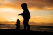 © Cavan Images - Two year old toddler stacking rocks on the beach at sunset.