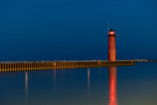Lighthouse On The Pier At Night With A Little Light Showing From The Beacon With Calm Waters.