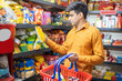 © GAJENDRRA BHATI  - Young Indian man buying grocery at shop or supermarket. Asian male choose snacks and food items while holding basket.
