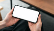 © patcharin.inn - Hands holding smartphone with mockup of blank screen on sofa in living room.