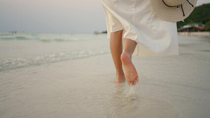 Wall Mural - Woman leg in white dress walking on the beach while travel tropical island on summer holiday vacation vacation at sunset. Attractive girl relax and enjoy outdoor lifestyle walking at seaside.