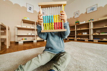 A child is playing with colorful abacus at kindergarten.