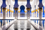 Fototapeta Sawanna - Symmetrical nightshot of the colonnade of the Sheik Zhayed mosque, with a marble catwalk surrounded by water