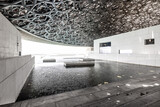 Fototapeta Sawanna - Atrium of the Louvre museum in Abu Dhabi, with latticework dome, marble walls and floor, and steps descending into the water