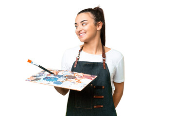 Young artist woman holding a palette over isolated chroma key background looking to the side and smiling