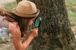 © _KUBE_ - Children's education. Curious little girl scout in a straw hat looks at trees bark through loupe. The concept of happy childhood