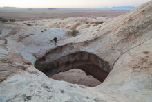 A Hiker Stands On The Edge Of The Giant Hole Eroded Into The Roof Of Wild Horse Window, San Rafael Swell, Utah.
