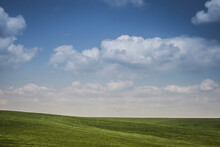 Rolling Green Hills And Blue Sky With Fluffy Clouds