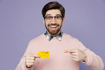 Poster - Surprised cool young caucasian IT man he wearing casual clothes pink sweater glasses hold point finger on mock up of credit bank card isolated on plain pastel light purple background studio portrait.