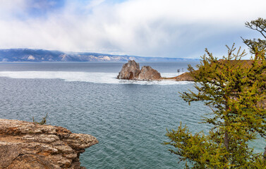 Baikal Lake on May day. Small Sea. View of natural attraction of Olkhon Island - Shamanka Rock or Burhan Cape. Beautiful spring landscape with melting ice floes on blue water and blooming larches 