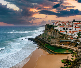Wall Mural - Amazing landscape of the Atlantic ocean shore in Azenhas do Mar village at sunset. View of of the sandy cove and dramatic cliffs. Big waves crashing into the rocky shore. Portugal.