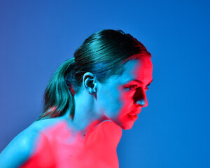 Poster - Head and shoulders close up portrait of pretty girl with expressive facial expressions, with  colourful neon gel lighting, isolated on studio background.