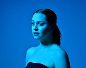 Wall Mural - Head and shoulders close up portrait of pretty girl with expressive facial expressions, with  colourful neon gel lighting, isolated on studio background.