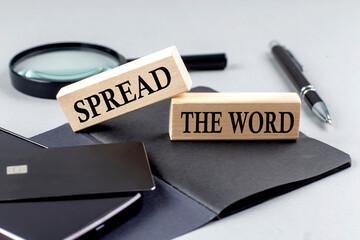 SPREAD THE WORD text on wooden block on black notebook , business concept