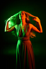 Sticker - portrait of pretty girl with blonde hair & elegant gown with expressive facial expressions & gestural arm poses. colourful neon gel lighting, isolated on black studio background.