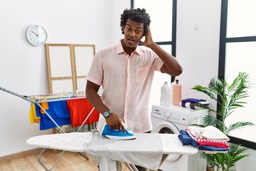 Poster - African man with curly hair ironing clothes at home crazy and scared with hands on head, afraid and surprised of shock with open mouth