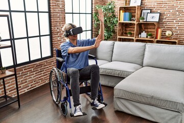 Poster - Young blond man playing video game using virtual reality glasses sitting on wheelchair at home