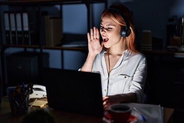 Canvas Print - Young caucasian woman working at the office at night shouting and screaming loud to side with hand on mouth. communication concept.