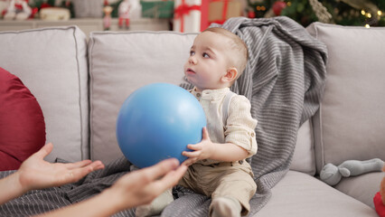 Sticker - Adorable toddler sitting on sofa by christmas tree with playing with ball at home