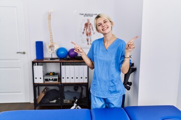 Poster - Young physiotherapist woman working at pain recovery clinic smiling confident pointing with fingers to different directions. copy space for advertisement