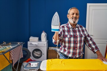 Canvas Print - Senior grey-haired man smiling confident holding iron machine at laundry room