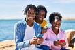 © Krakenimages.com - African american friends using smartphone sitting on rock at seaside