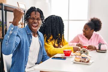 Poster - Group of three young black people sitting on a table having coffee annoyed and frustrated shouting with anger, yelling crazy with anger and hand raised