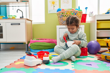 Wall Mural - Adorable hispanic toddler playing with supermarket toy sitting on floor at kindergarten