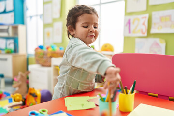 Wall Mural - Adorable hispanic toddler student drawing on paper standing at kindergarten