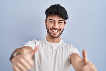 Canvas Print - Hispanic man with beard standing over white background approving doing positive gesture with hand, thumbs up smiling and happy for success. winner gesture.