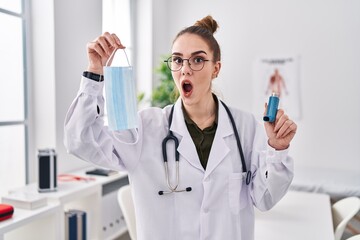 Sticker - Young hispanic girl holding medical asthma inhaler at the clinic afraid and shocked with surprise and amazed expression, fear and excited face.