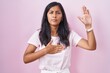 © Krakenimages.com - Young hispanic woman standing over pink background swearing with hand on chest and open palm, making a loyalty promise oath