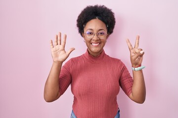 Sticker - Beautiful african woman with curly hair standing over pink background showing and pointing up with fingers number seven while smiling confident and happy.