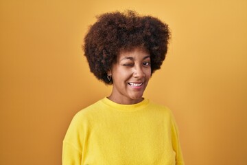 Canvas Print - Young african american woman standing over yellow background winking looking at the camera with sexy expression, cheerful and happy face.