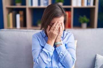 Sticker - Middle age hispanic woman sitting on the sofa at home with sad expression covering face with hands while crying. depression concept.