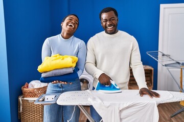 Poster - Young african american couple ironing clothes at laundry room celebrating crazy and amazed for success with open eyes screaming excited.